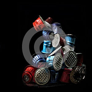Pile of colorful used coffee capsules against a black background, a lot of unnecessary waste from disposable packaging made from