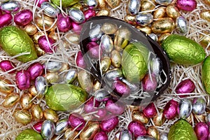 Pile of colourful foil wrapped chocolate easter eggs in green, pink, yellow and gold with half of a large brown dark chocolate egg