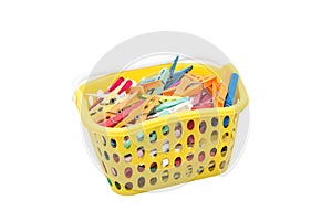 Pile of colourful plastic cloth clamps inside yellow basket isolated on white background.