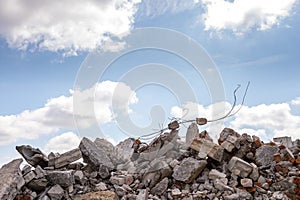 A pile of concrete fragments of a destroyed building with protruding rebar against the blue sky. Background