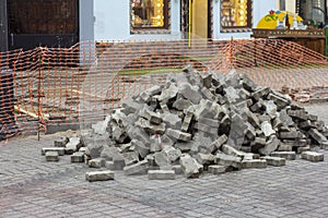 A pile of concrete stones on a construction site with a fence. Paving stones for the repair and laying of the sidewalk