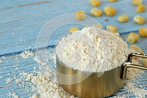 Pile of corn flour in golden measuring cup on wooden table, close-up