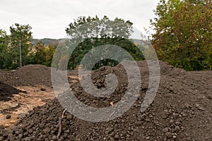 Pile of dark construction gardening soil mud land earth dirt heap pile mound, freshly dug, with some wet soil and leaves