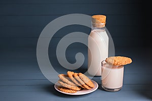 A pile of delicious homemade cookies on a white plate, a bottle of milk and a glass of milk on a blue wooden background