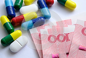 Pile of different colouful pills placed next to 100 yuan banknotes. Illustrative for cost of medical bills, health insurance and o