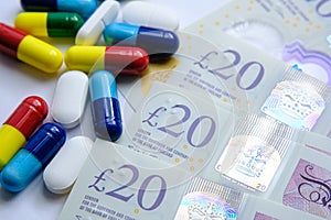 Pile of different colouful pills placed next to 20 british pound banknotes. Illustrative for cost of medical bills, health insuran