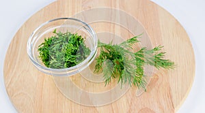 Pile of dill leaves in glass bowl and dill twigs on round wooden