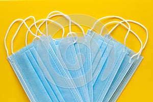 Pile of disposable medical face masks on yellow background. Personal protective equipment, PPE