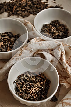 Pile of dried green tea leaves in little bowls, white background, dried tea leaves