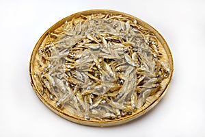 Pile of dried minnow fishes in bamboo basket on white background