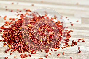 Pile of dried red hot chilly flakes on light wooden background, top view, close-up, macro, shallow depth of field.