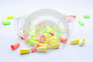 Pile of earplugs against noise in different colors and plastic transparent protective work goggles.