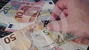 On a pile of euro banknotes, a hand lays a black dice with the number 4 on top