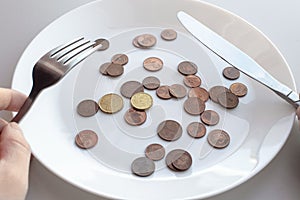 Pile of euro coins lie on a plate. Male hands hold cutlery knife and fork to start eating a dish. View from above