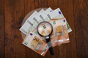 Pile of European money under a magnifying glass on wooden background