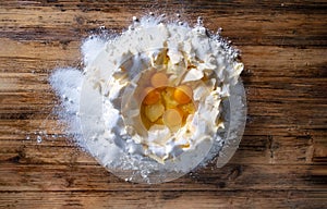 a pile of flour, eggs, margarine, sugar on a wooden table to knead dough to bake Christmas cookies