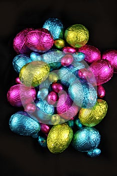 Pile of foil wrapped chocolate easter eggs in pink, blue & lime green