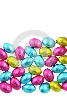 Pile of foil wrapped chocolate easter eggs in pink, blue & lime green with a white background