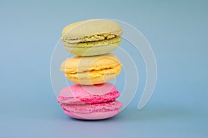 Pile of french green, yellow and pink round macarons with fillers on blue background with copy space