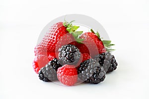 Pile of fresh berries on a white background including strawberries, blackberries and raspberries