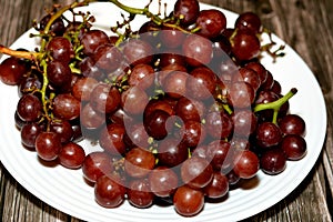 pile of fresh red grapes fruit isolated on white plate isolated on wooden background, selective focus of a bunch of red grapes,