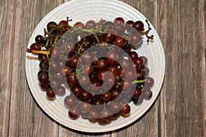 pile of fresh red grapes fruit isolated on white plate isolated on wooden background, selective focus of a bunch of red grapes,