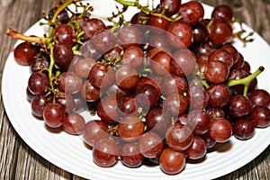 pile of fresh red grapes fruit isolated on white plate isolated on wooden background, selective focus of a bunch of red grapes,