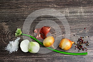 Pile of fresh spring golden and green onion with peel, white salt, black pepper on wooden background