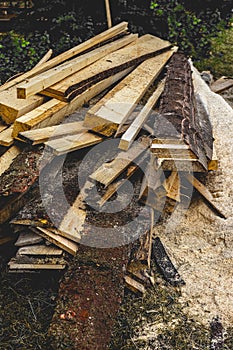 Pile of freshly sawn boards with different cross sections and a mountain sawdust on a meadow, close-up