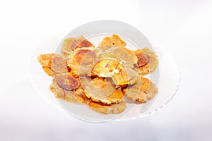 Pile of fried and smashed bananas on white background. Patacones, Tostones, chips, ripe plantain. On a white plate.