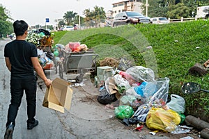 Pile of garbage bags and messy trash on street sidewalk with traffic on background in Hanoi, Vietnam. A man dumping rubbish into