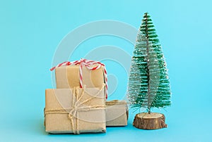Pile of gift boxes wrapped in craft paper tied with twine red white ribbon Christmas tree on mint blue background. New Year
