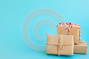 Pile of gift boxes wrapped in craft paper tied with twine red white ribbon on mint light blue background. New Year Christmas