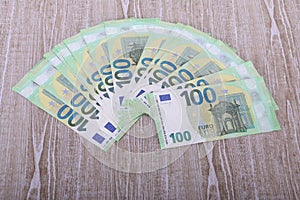 pile of green 100 euro bills lie spread out like a fan on a wooden table