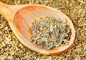 Pile of ground dried Basil (Sweet Basil) as background with wooden spoon. Used as a spice in culinary herb all over the world.