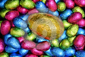 Pile or group of multi colored and different sizes of colourful foil wrapped chocolate easter eggs in pink, blue, yellow and lime