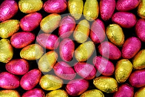 Pile or group of multi colored and different sizes of foil wrapped chocolate easter eggs in yellow, gold and pink