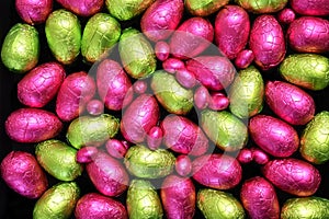 Pile or group of multi coloure and different sizes of colourful foil wrapped chocolate easter eggs in lime green; yellow, and pink