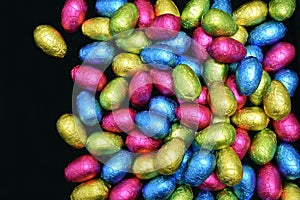 Pile or group of multi coloure and different sizes of colourful foil wrapped chocolate easter eggs in pink, blue, yellow and lime.