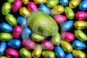 Pile or group of multi coloured & different sizes of colourful foil wrapped chocolate easter eggs in pink, blue, yellow and lime.