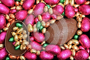 Pile or group of multi coloured and different sizes of colourful foil wrapped chocolate easter eggs in pink, red, gold and lime.