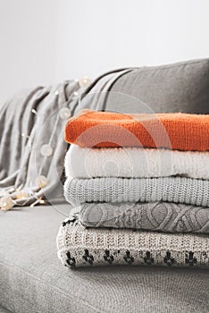 Pile of handmade warm sweaters of gray, white and orange color on sofa bed