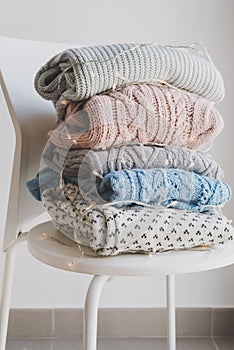 Pile of handmade woolen sweaters on white chair and decorative lights