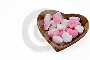 pile of heart shaped sugar Candies on a heart shaped wooden bowl isolated on a white background