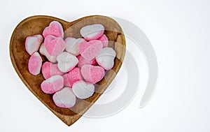pile of heart shaped sugar Candies on a heart shaped wooden bowl isolated on a white background