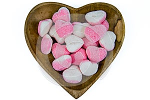 pile of heart shaped sugar Candies on a heart shaped wooden bowl isolated on a white background