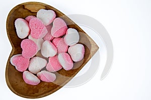 pile of heart shaped sugar Candies on a heart shaped wooden bowl isolated on a white background