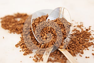 Pile of instant coffee grains in metal spoons, over marbble surface. Caffiene drink.