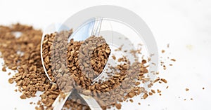 Pile of instant coffee grains on silver spoon, over marbble surface. Caffiene drink. Banner.