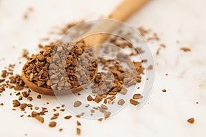 Pile of instant coffee grains in wooden spoon, over marbble surface. Caffiene drink. Copy space.